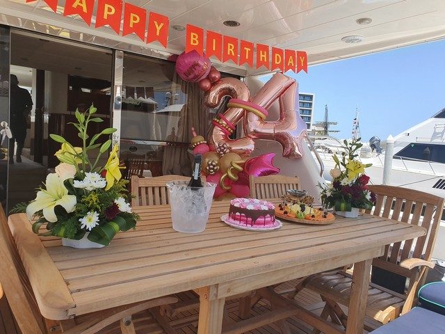 Birthday table with flowers, balloons and a cake on a yacht deck
