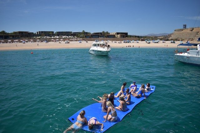Guests on a floating water mat beside an anchored yacht