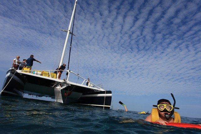 Snorkeler in a mask and life vest beside a sailing catamaran