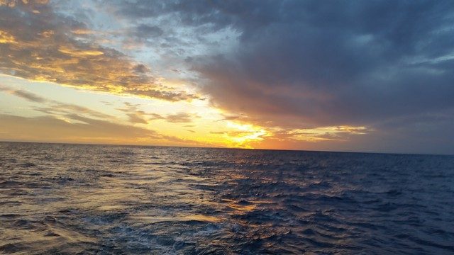 Sun setting over the ocean beneath dramatic clouds