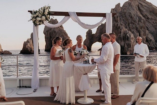 Wedding ceremony under a floral arch on a boat in front of Land's End
